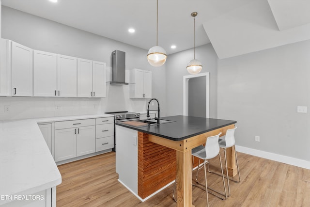 kitchen featuring wall chimney exhaust hood, sink, a kitchen island with sink, and white cabinets