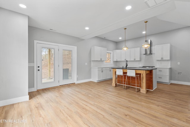 kitchen featuring a breakfast bar area, white cabinetry, a center island with sink, wall chimney exhaust hood, and light wood-type flooring