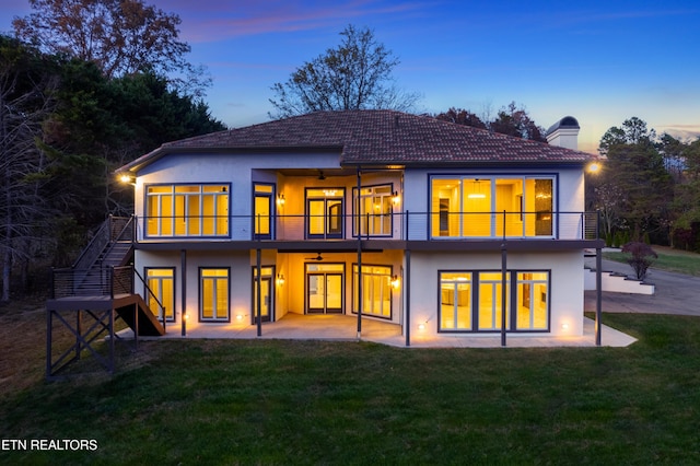 back house at dusk featuring a yard, a balcony, and a patio area