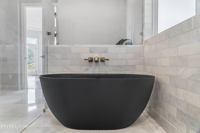 bathroom with a tub to relax in and tile walls