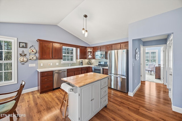 kitchen with wooden counters, appliances with stainless steel finishes, tasteful backsplash, hanging light fixtures, and a center island