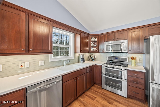 kitchen with lofted ceiling, decorative backsplash, sink, light hardwood / wood-style flooring, and appliances with stainless steel finishes