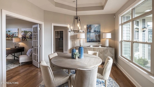 dining space with a raised ceiling, ornamental molding, a notable chandelier, and dark hardwood / wood-style flooring