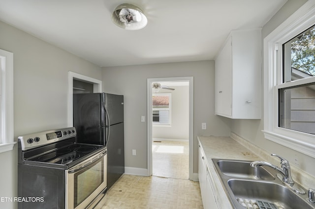 kitchen featuring stainless steel electric range oven, sink, black fridge, light parquet floors, and white cabinets