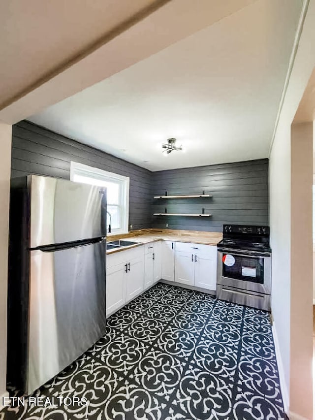 kitchen featuring white cabinets, appliances with stainless steel finishes, sink, and wooden walls