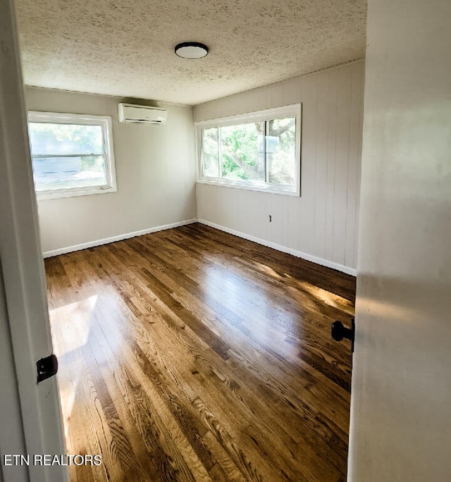 empty room with a wall mounted air conditioner, a textured ceiling, and wood-type flooring