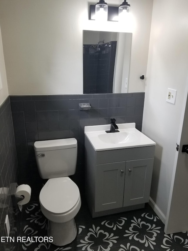 bathroom with tile patterned floors, vanity, tile walls, toilet, and a tile shower