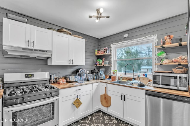 kitchen featuring sink, stainless steel appliances, wood walls, and white cabinets