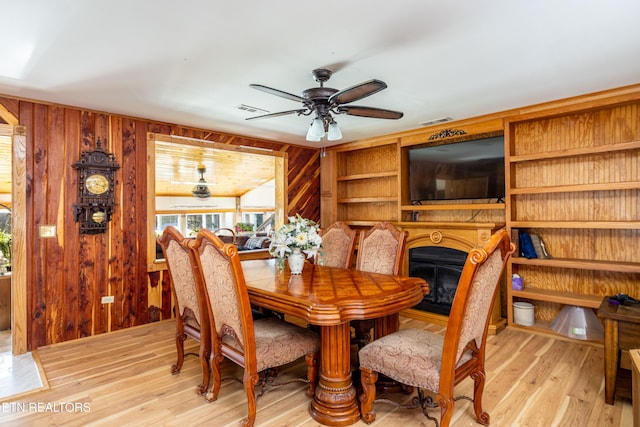 dining space with wood walls, ceiling fan, and light hardwood / wood-style floors