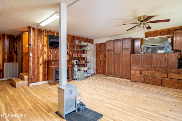 living room with a fireplace, a textured ceiling, light hardwood / wood-style flooring, and wooden walls