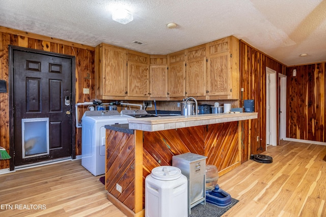 clothes washing area with wood walls, light hardwood / wood-style floors, and a textured ceiling