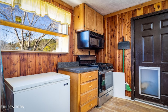 kitchen with refrigerator, light hardwood / wood-style floors, wooden walls, and stainless steel range with gas stovetop