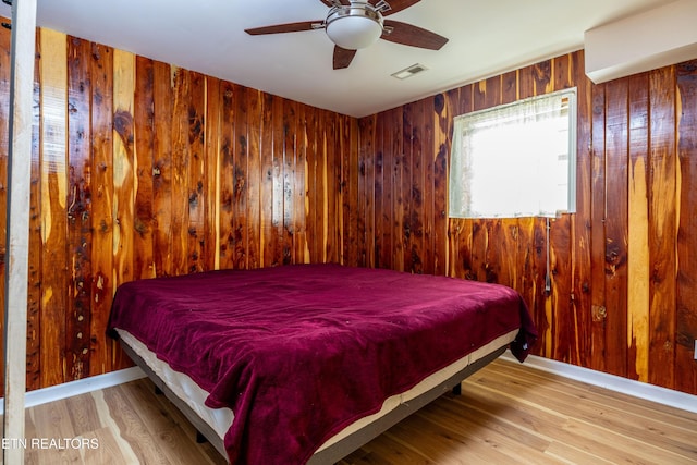 bedroom featuring ceiling fan, wooden walls, and light hardwood / wood-style flooring