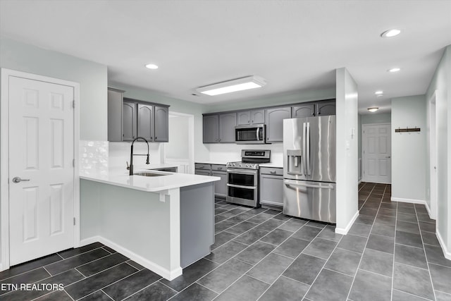 kitchen featuring kitchen peninsula, a kitchen bar, stainless steel appliances, sink, and gray cabinets