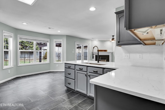 kitchen featuring ceiling fan, sink, kitchen peninsula, gray cabinets, and decorative backsplash