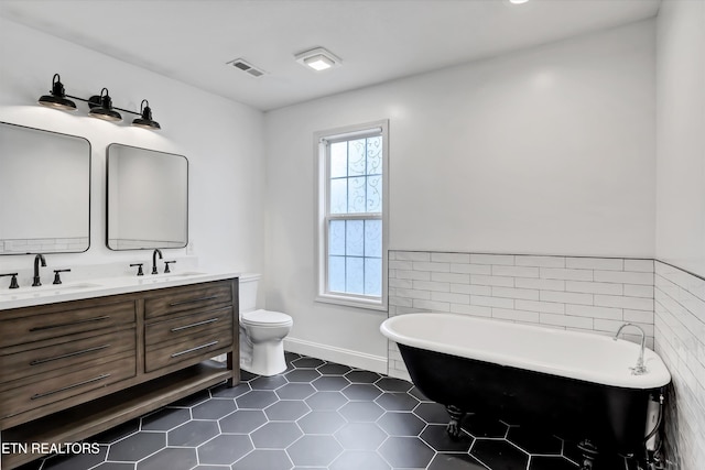 bathroom with tile patterned floors, a bathtub, vanity, tile walls, and toilet