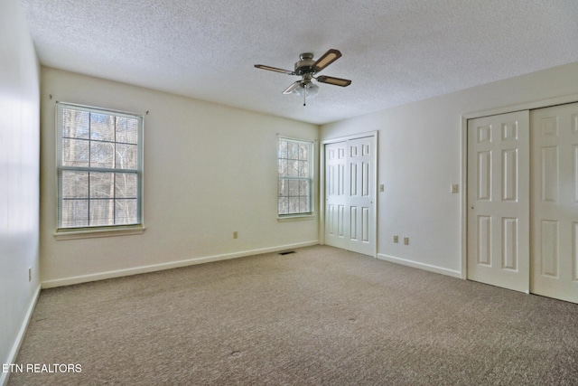 unfurnished bedroom with multiple closets, ceiling fan, light colored carpet, and a textured ceiling