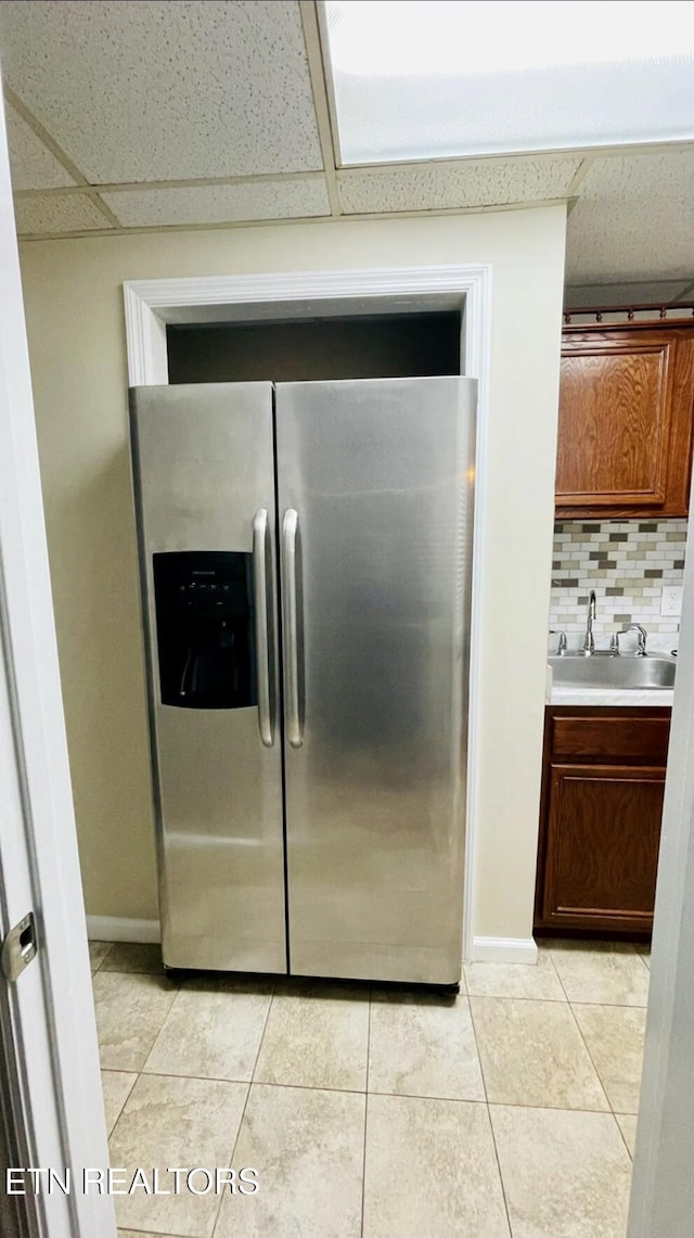 interior space featuring a drop ceiling, sink, decorative backsplash, stainless steel fridge, and light tile patterned floors