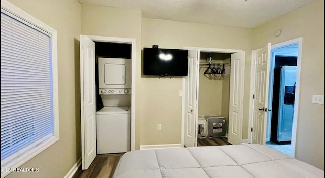 bedroom featuring stainless steel fridge, stacked washing maching and dryer, a textured ceiling, connected bathroom, and dark hardwood / wood-style flooring