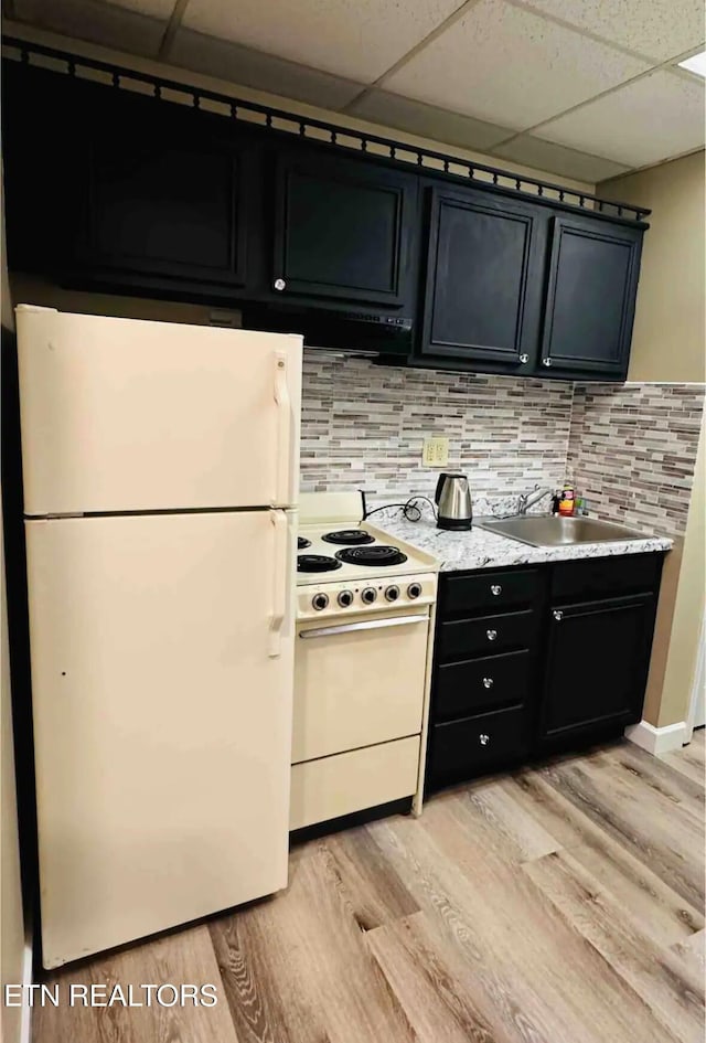 kitchen featuring a paneled ceiling, white appliances, sink, light hardwood / wood-style flooring, and tasteful backsplash