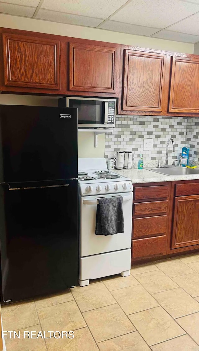 kitchen featuring sink, black fridge, white range with electric stovetop, backsplash, and a paneled ceiling