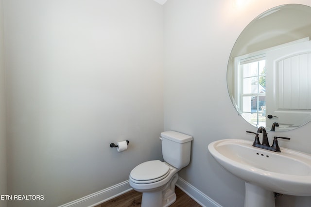 half bathroom featuring wood finished floors, a sink, toilet, and baseboards