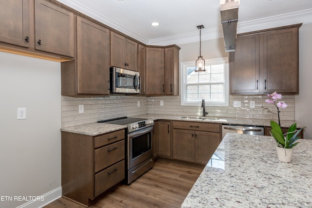 kitchen featuring light stone counters, crown molding, appliances with stainless steel finishes, a sink, and wood finished floors