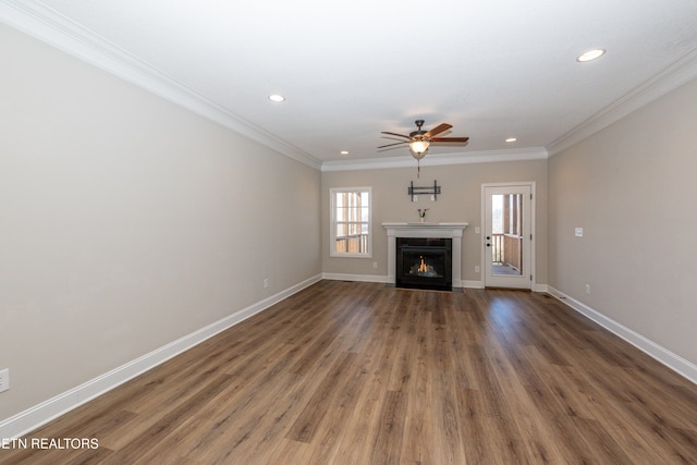 unfurnished living room with a warm lit fireplace, recessed lighting, wood finished floors, baseboards, and crown molding