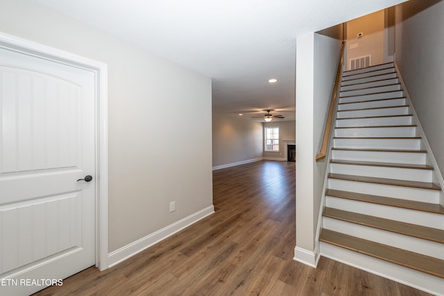 stairs with baseboards, visible vents, a ceiling fan, wood finished floors, and a fireplace