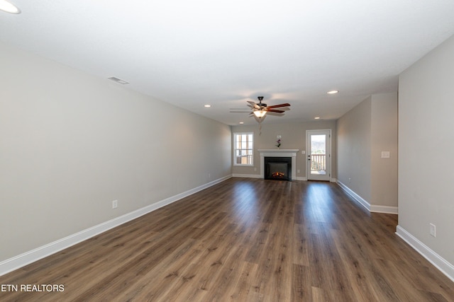 unfurnished living room featuring dark wood-style floors, recessed lighting, a warm lit fireplace, and baseboards