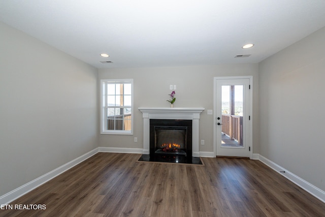 unfurnished living room featuring a fireplace with flush hearth, a wealth of natural light, visible vents, and wood finished floors