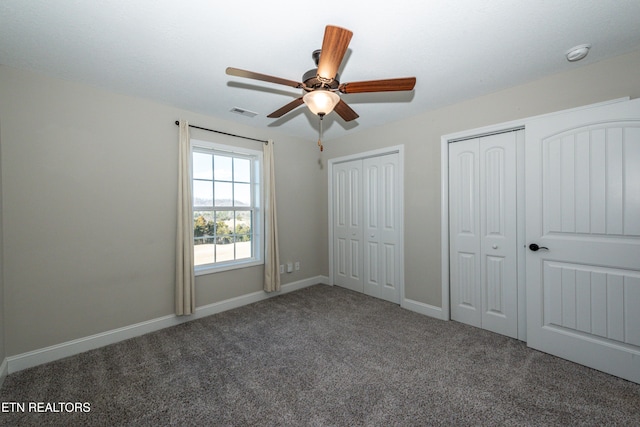 unfurnished bedroom featuring multiple closets, visible vents, carpet flooring, ceiling fan, and baseboards