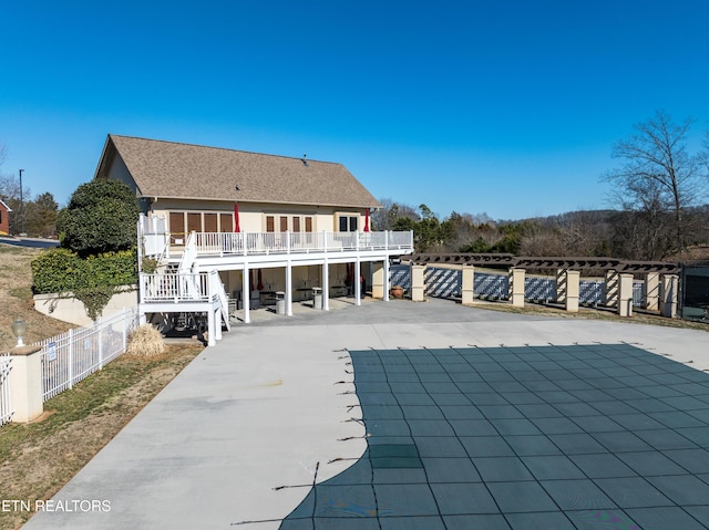 rear view of property with fence, stairs, driveway, roof with shingles, and a patio area