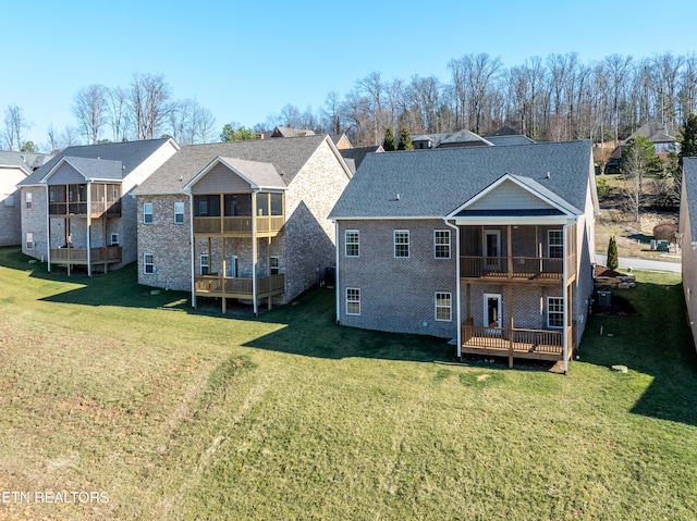 back of property featuring a yard, brick siding, a wooden deck, and a balcony