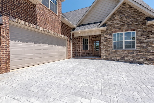 view of front of property with stone siding, decorative driveway, brick siding, a garage, and a shingled roof