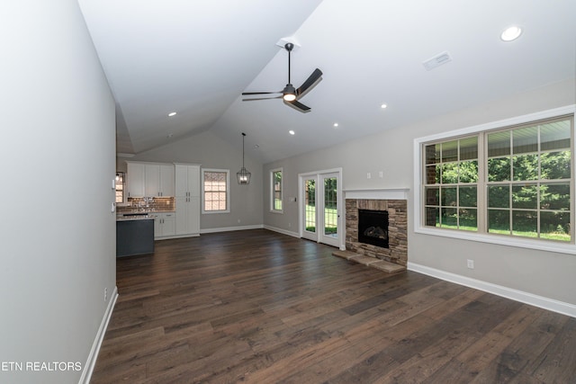 unfurnished living room with a stone fireplace, baseboards, a ceiling fan, and dark wood-style floors