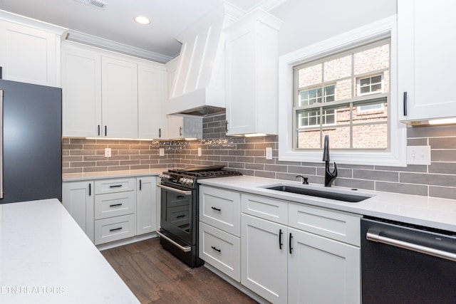 kitchen with freestanding refrigerator, dishwashing machine, light countertops, a sink, and stainless steel gas range oven