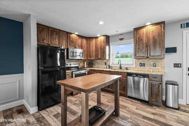 kitchen with light stone counters, sink, light hardwood / wood-style flooring, and appliances with stainless steel finishes