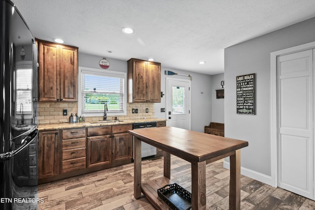 kitchen featuring sink, black fridge, light stone counters, backsplash, and dishwashing machine