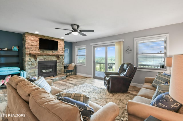 living room featuring a stone fireplace, ceiling fan, and light hardwood / wood-style floors