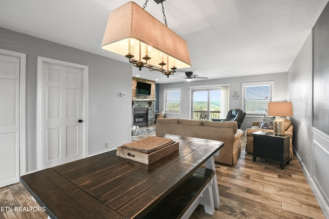 dining area featuring a fireplace, ceiling fan with notable chandelier, and hardwood / wood-style flooring