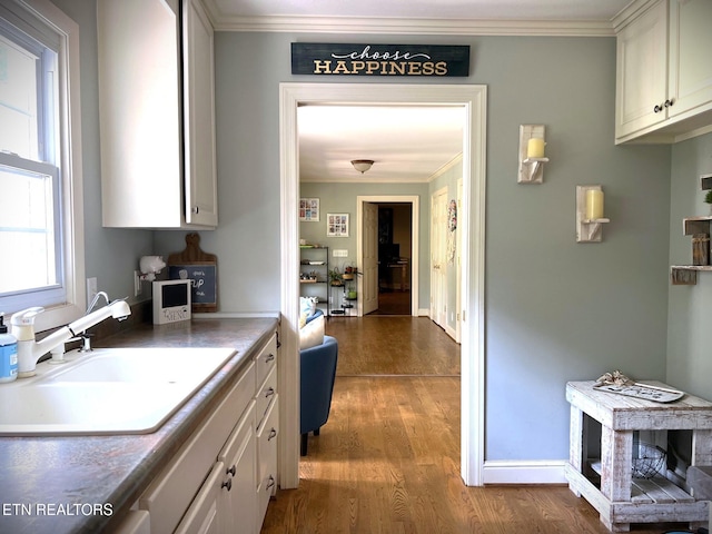 kitchen with ornamental molding, sink, hardwood / wood-style floors, and white cabinets