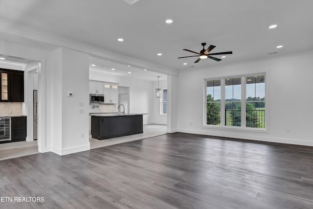 unfurnished living room featuring wine cooler, ceiling fan, dark wood-type flooring, and sink