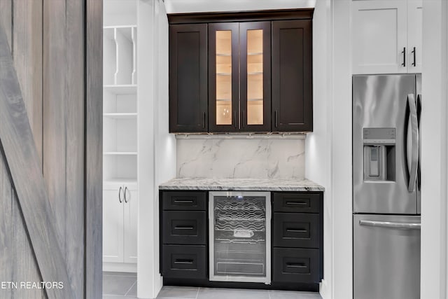 kitchen featuring backsplash, light stone countertops, dark brown cabinets, and stainless steel refrigerator with ice dispenser