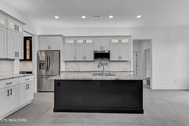 kitchen with white cabinetry, sink, stainless steel appliances, light stone counters, and a kitchen island with sink