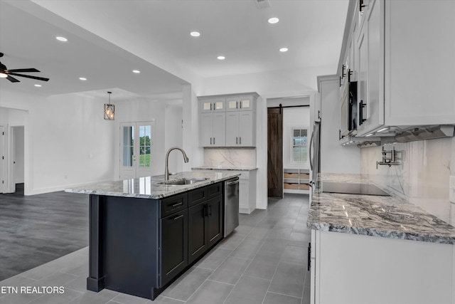 kitchen with sink, a barn door, stainless steel dishwasher, a kitchen island with sink, and white cabinets