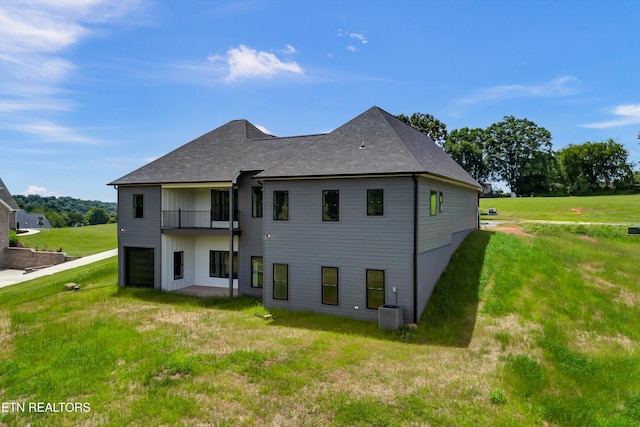 rear view of property with a garage, a yard, a balcony, and central AC