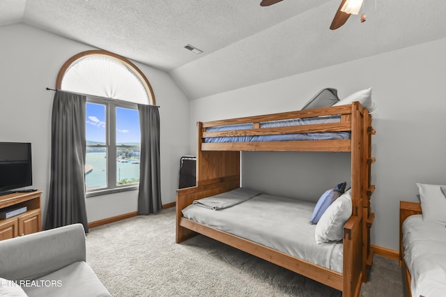 carpeted bedroom with a water view, ceiling fan, vaulted ceiling, and a textured ceiling