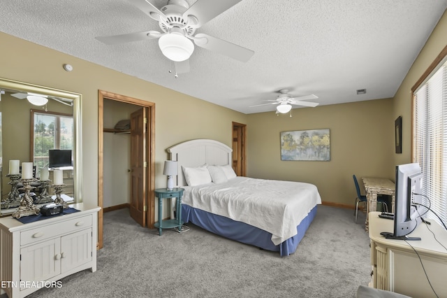 carpeted bedroom with ceiling fan, a spacious closet, and a textured ceiling