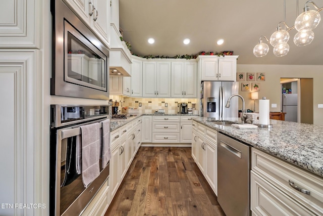 kitchen with sink, light stone countertops, appliances with stainless steel finishes, decorative light fixtures, and white cabinetry